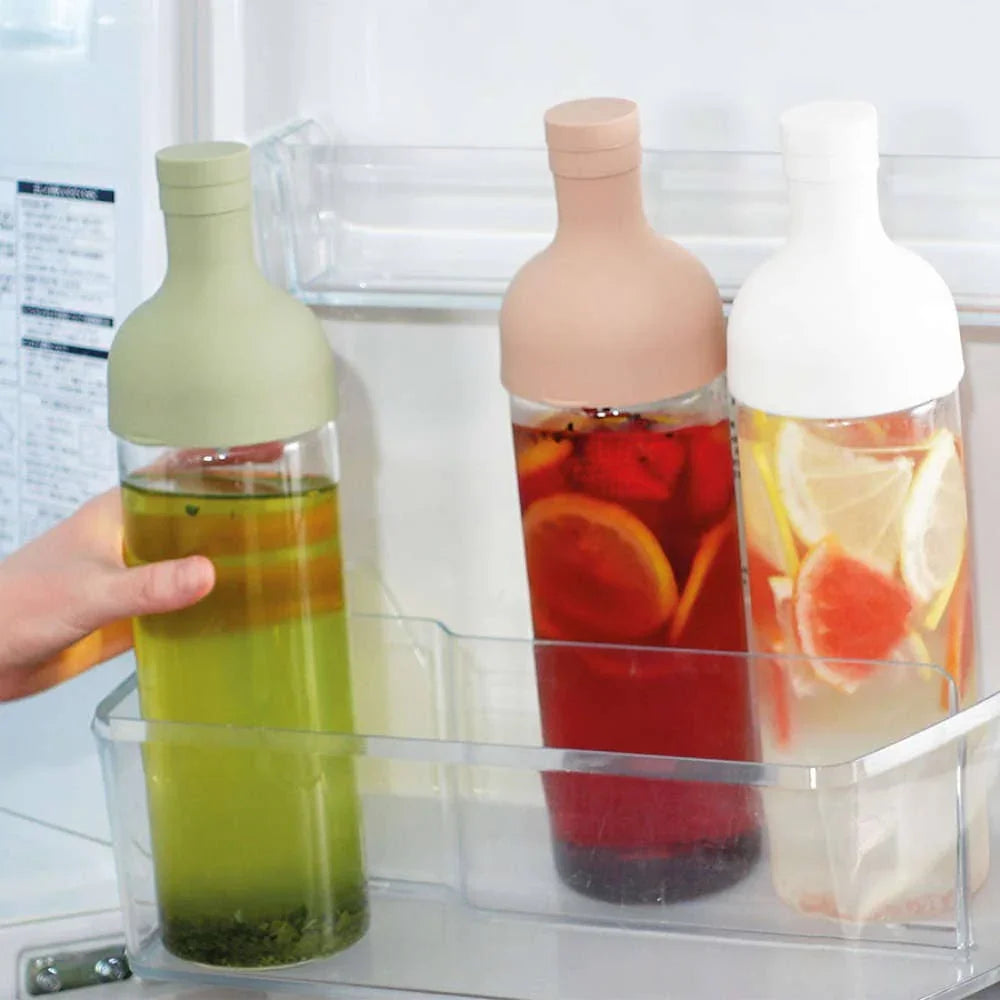 Drie glazen flessen met siliconen doppen in koelkastdeur met infused water en fruit