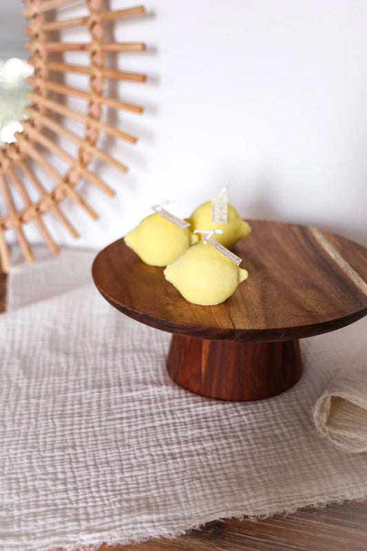 Drie gele citroen kaarsen op een ronde houten standaard, witte textiel ondergrond