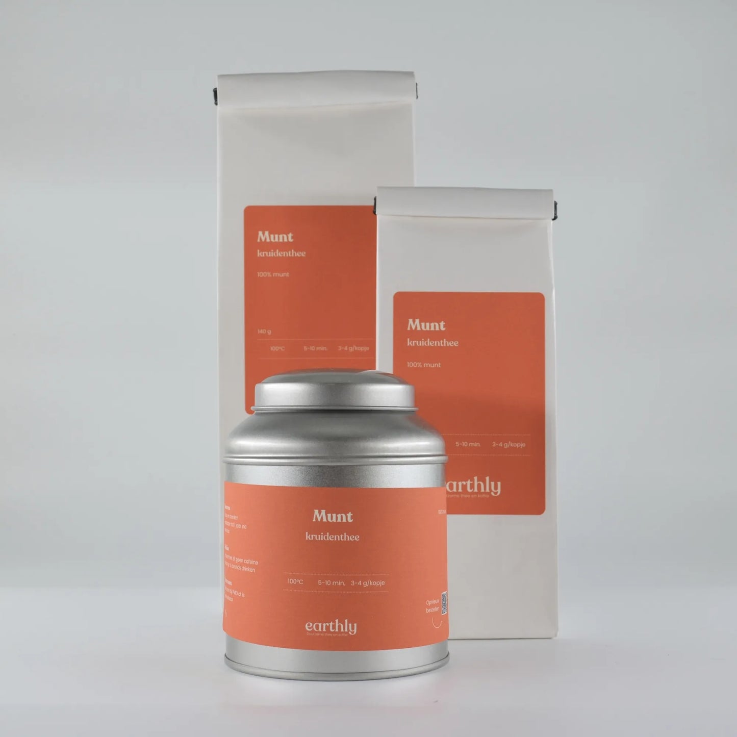 Zilverkleurige theeblik en witte zakken met oranje etiketten van aardse munt kruidenthee