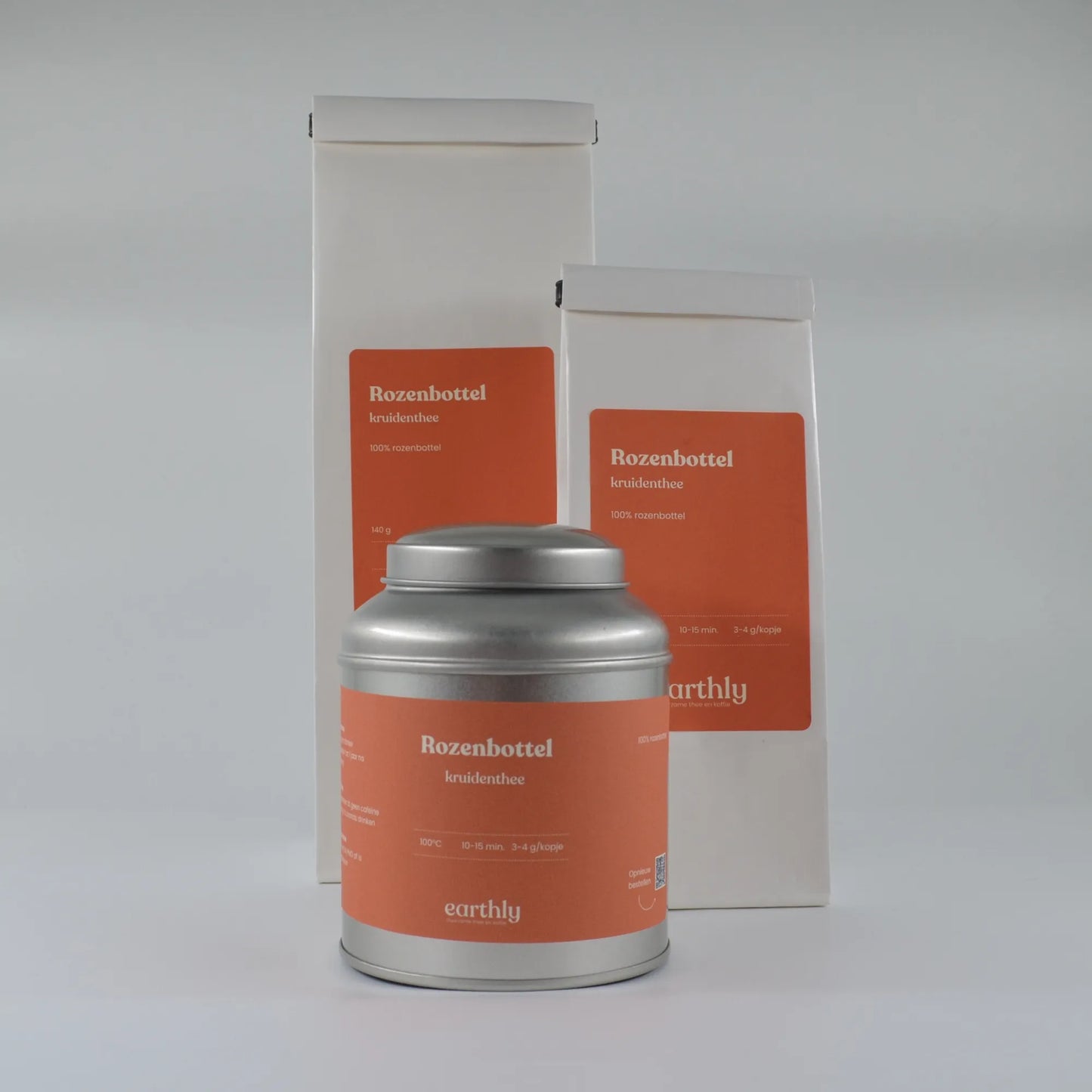 Zilver blik en twee witte zakken met oranje etiketten Rozenbottel kruidenthee van Earthly